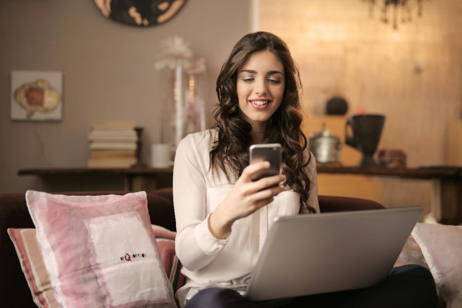 Woman on couch looking at phone and laptop